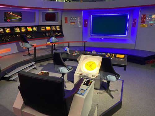 A futuristic control room with sleek chairs, colorful screens, and a central console, resembling a sci-fi spaceship bridge.