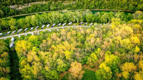 Aerial view of a winding road lined with RVs, surrounded by lush green trees and a river.
