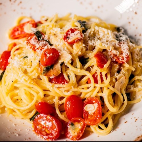 A plate of spaghetti topped with cherry tomatoes, herbs, and grated cheese, served in a white bowl.