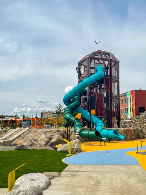 Colorful playground featuring a large turquoise slide, rock formations, and vibrant structures under a cloudy sky.