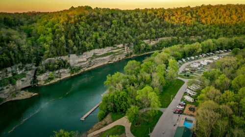 Aerial view of a river surrounded by lush greenery, with a campground and parked RVs along the shore.