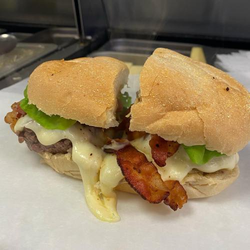 A close-up of a sandwich with bacon, green peppers, and melted cheese on a soft bun, resting on parchment paper.