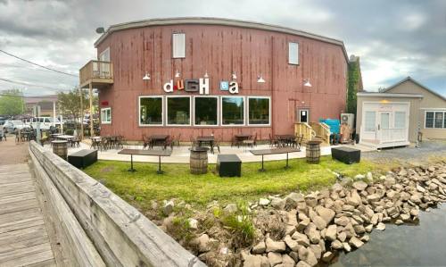 A rustic red building with large windows, outdoor seating, and a waterfront view, featuring the sign "dug ha."