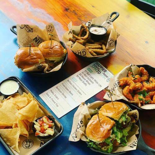 A colorful spread of burgers, onion rings, and nachos with salsa on a vibrant table, alongside a menu.