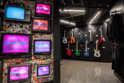 A vibrant music store interior featuring colorful guitars on a wall and retro TVs displaying "KRAMER" logos.