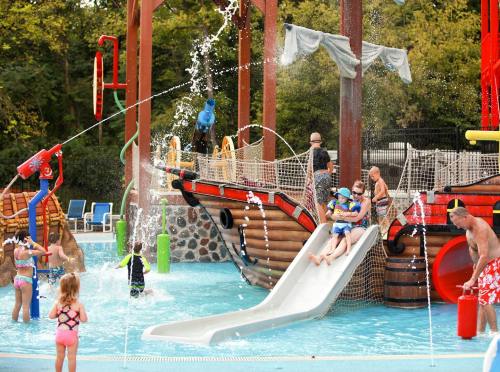 Children and adults enjoy a water park with a pirate ship, slides, and water sprays on a sunny day.