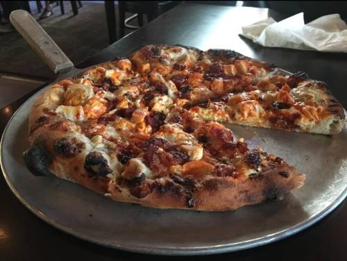 A freshly baked pizza on a metal tray, topped with cheese, chicken, and a crispy crust, with one slice removed.