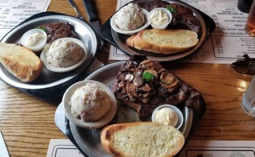 Three plates of hearty meals featuring steak, mashed potatoes, and toasted bread, served in a casual dining setting.