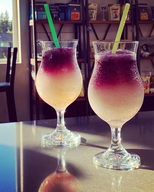 Two colorful cocktails with gradient layers, served in elegant glasses with green straws, on a countertop.
