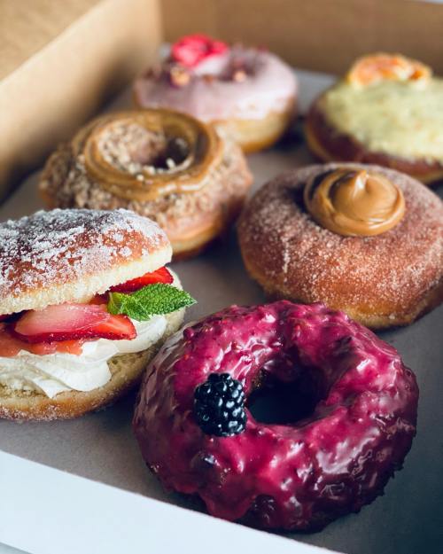 A box of assorted donuts, including a strawberry cream donut and a berry-glazed donut, with various toppings.