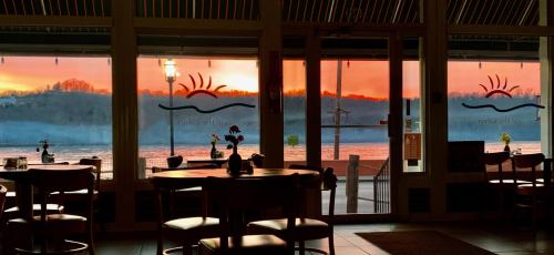 A cozy restaurant interior with tables, showcasing a vibrant sunset over a lake through large glass doors.