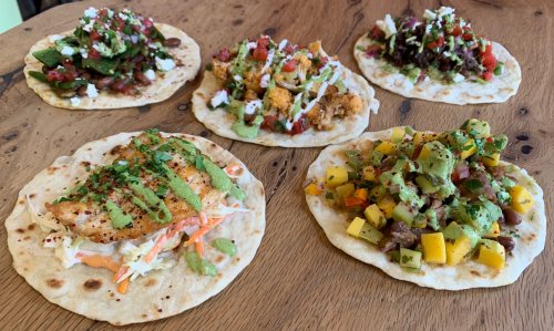 A variety of colorful tacos on tortillas, topped with fresh ingredients like salsa, avocado, and herbs, on a wooden table.