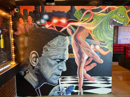 A vibrant mural featuring Frankenstein, a ghostly figure, and playful characters in a colorful, urban setting.