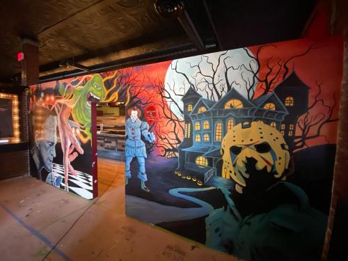 A vibrant mural featuring iconic horror characters and a spooky haunted house against a dramatic sunset backdrop.