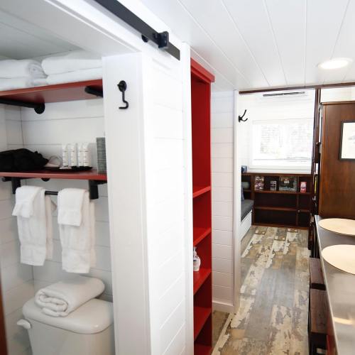 Bright, modern bathroom with white shelves, neatly arranged towels, and a cozy seating area visible in the background.