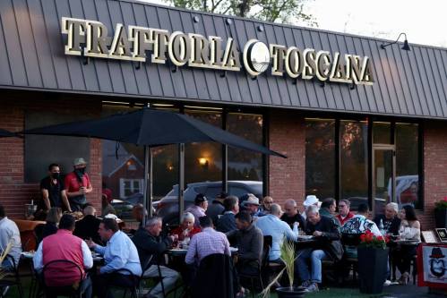Outdoor dining scene at Trattoria Toscana, with patrons enjoying meals under umbrellas in a lively atmosphere.