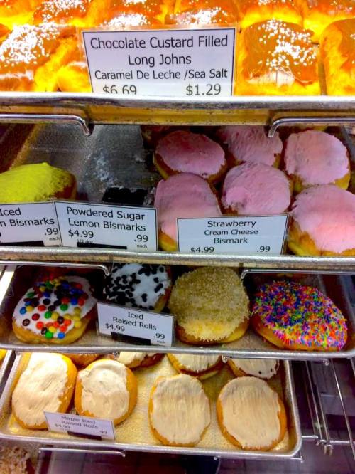 A display of various donuts, including long johns, bismarks, and iced rolls, with price tags visible.
