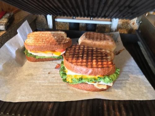 Two grilled sandwiches with lettuce, tomato, cheese, and turkey on parchment paper, with grill marks visible.
