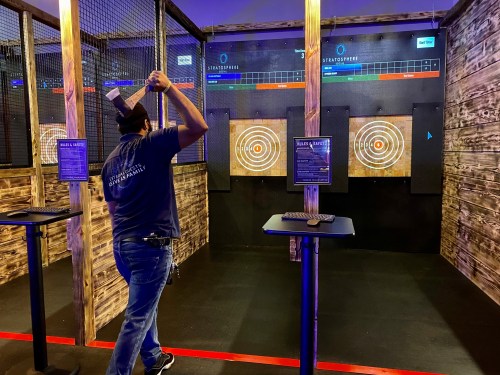 A person prepares to throw an axe at targets in a dimly lit axe-throwing venue with wooden decor.