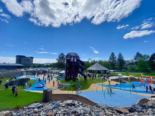 A vibrant playground with slides, climbing structures, and children playing under a blue sky with scattered clouds.