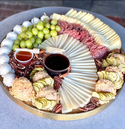 A beautifully arranged charcuterie board with cheeses, meats, grapes, pickles, nuts, and dipping sauces.