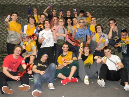 A large group of people in matching yellow shirts, holding toy guns and posing together in a playful setting.