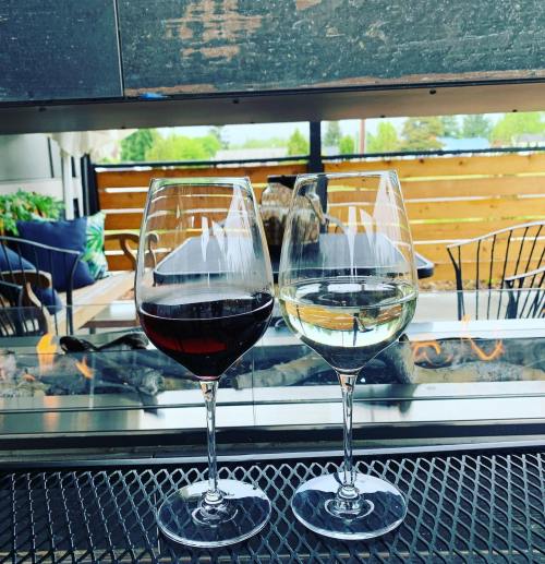 Two wine glasses, one filled with red wine and the other with white, sit on a table by a cozy fireplace.