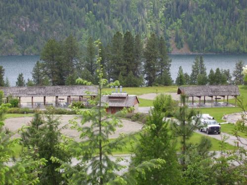 A scenic view of a lake surrounded by trees, with rustic buildings and parked cars in the foreground.