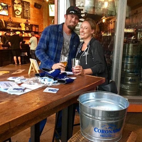 A couple smiles while holding drinks at a bar, with a bucket of ice and beer bottles on the table.