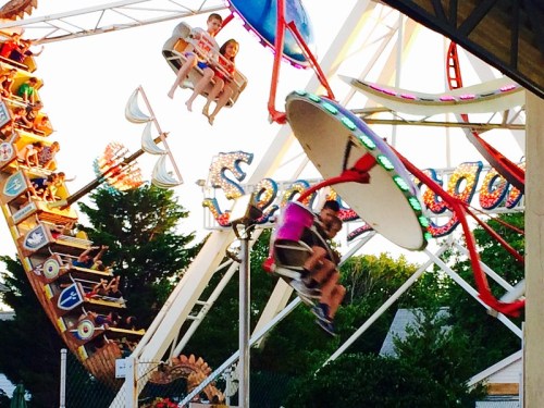 A vibrant amusement park scene with riders enjoying spinning rides and a colorful Ferris wheel in the background.