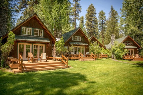 A row of charming cabins with porches, surrounded by lush green grass and tall trees under a clear blue sky.