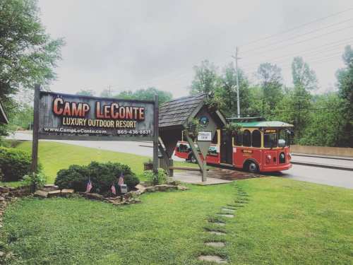 A red trolley bus parked near the Camp LeConte sign at a luxury outdoor resort, surrounded by greenery.