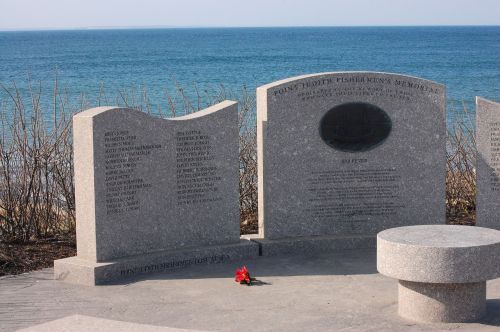 A memorial by the water honoring Point Judith fishermen, featuring engraved names and a flower placed at the base.