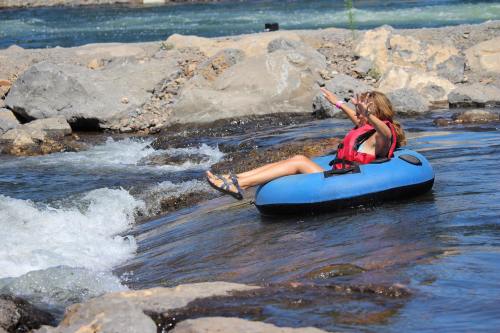 A person in a red life jacket relaxes on a blue inner tube, floating down a river with rocky banks.