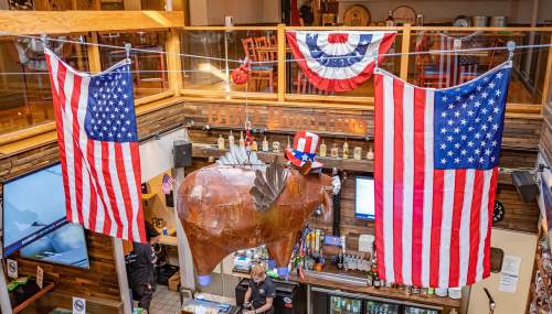 A large metal pig wearing a hat hangs from the ceiling, surrounded by American flags in a festive bar setting.