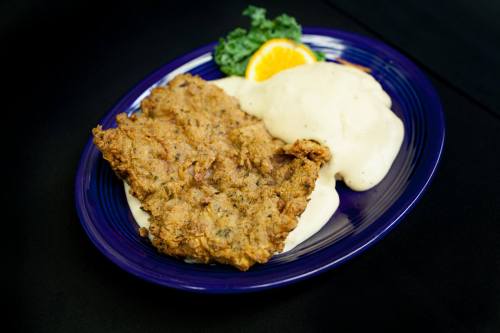 A plate of fried chicken with creamy gravy, served with mashed potatoes and a slice of orange on the side.