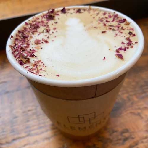 A cup of latte topped with rose petals, resting on a wooden surface.