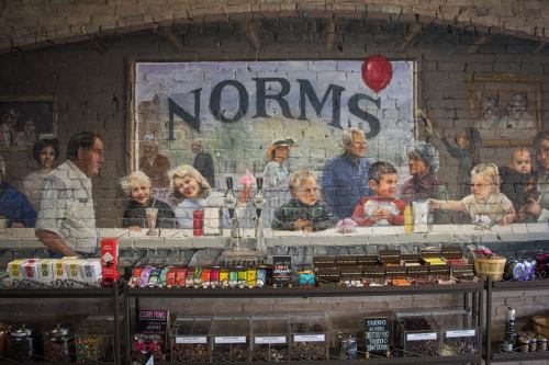 A mural depicting a nostalgic scene at a diner, with people enjoying ice cream and a large "NORMS" sign above.