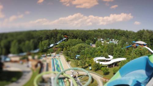 Aerial view of a water park featuring slides, pools, and lush greenery under a partly cloudy sky.