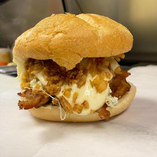 A close-up of a sandwich with crispy chicken, cheese, and crunchy toppings, served on a soft bun.