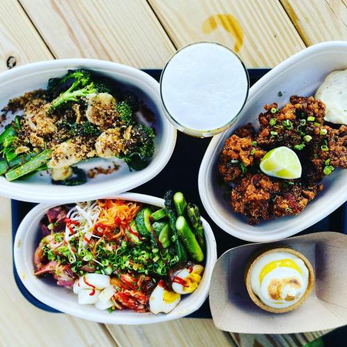 A platter featuring broccoli, fried chicken with lime, colorful salads, and a dessert, accompanied by a glass of beer.