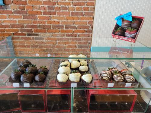 A display of chocolate-covered strawberries in dark and white chocolate, arranged neatly in a glass case.