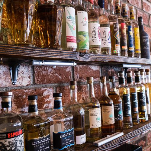 A wooden shelf displaying a variety of liquor bottles against a brick wall.