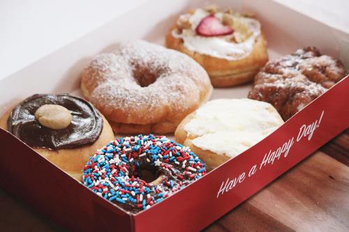 A box of assorted donuts, including a chocolate frosted, a glazed, and one with sprinkles, with a cheerful message.