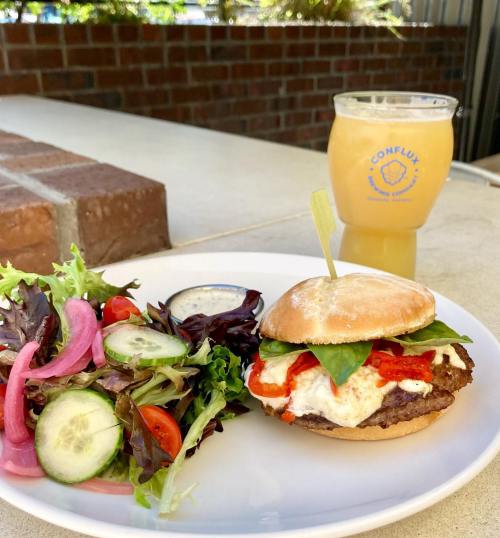 A burger with toppings, served with a side salad and a glass of lemonade on a table.
