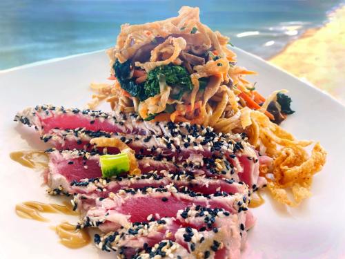 A plate of seared tuna steak, sliced and topped with sesame seeds, served with a colorful vegetable salad.