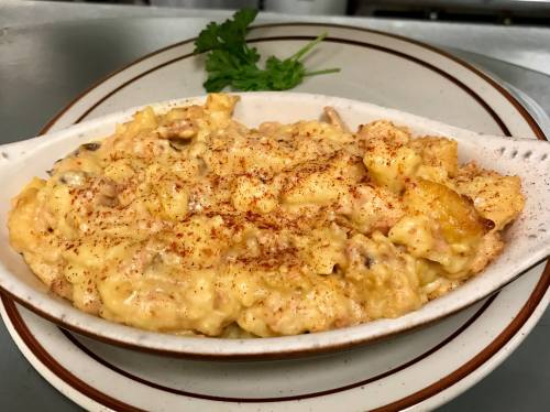 Creamy macaroni and cheese topped with paprika, served in a white dish with a sprig of cilantro on the side.