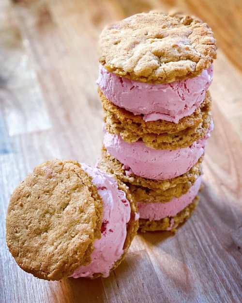 A stack of ice cream sandwiches with pink ice cream between two golden cookies, set on a wooden surface.