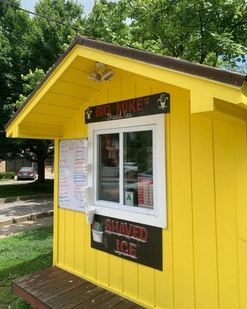 A bright yellow shack with a sign reading "Big Mike's Shaved Ice" and a menu displayed on the side.