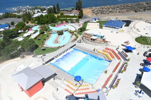 Aerial view of a water park featuring a wave pool, lazy river, and colorful lounge chairs under sunny skies.